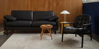 Schwarzes Ledersofa mit Sessel, Flechttisch und Lampe vor Holzpaneelwand